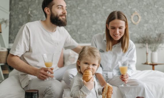 A family enjoying breakfast in their bedroom, featuring croissants and orange juice.