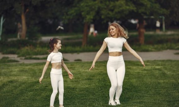 Mother and daughter bonding through outdoor exercise in activewear, featuring a joyful moment in a green park.